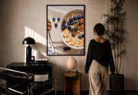 Blueberry Banana Oatmeal Bowl print in a black frame on a sunlit plaster wall, a woman looking on beside a mushroom lamp