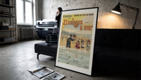 Woman and children wading at beach print in a slim black frame leaning on a dark sofa in a concrete print studio