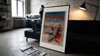 Woman in traditional dress by seaside print in a slim black frame leaning on a dark sofa in a concrete print studio