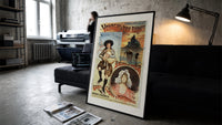 Breton bagpiper and young woman print in a slim black frame leaning on a dark sofa in a concrete print studio