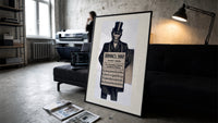 Monkey in top hat and suit print in a slim black frame leaning on a dark sofa in a concrete print studio
