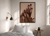 Brown French Tips print in a black frame above a bed with striped linens, a brass wall lamp and a sunlit window