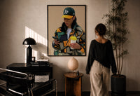 Camo Jacket and Takeaway Drink print in a black frame on a sunlit plaster wall, a woman looking on beside a mushroom lamp