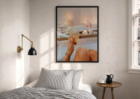 Candlelit Bath with a Drink print in a black frame above a bed with striped linens, a brass wall lamp and a sunlit window
