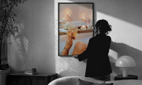 Candlelit Bath with a Drink print in a slim black frame being hung on a sunlit wall in a monochrome room