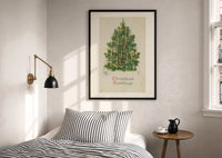 Christmas Tree Greetings print in a black frame above a bed with striped linens, a brass wall lamp and a sunlit window