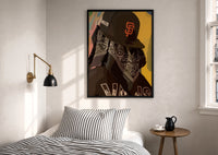 Cap and Paisley Bandana print in a black frame above a bed with striped linens, a brass wall lamp and a sunlit window