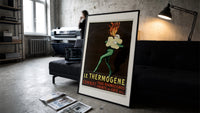 Fire-breathing man clutching cotton wool print in a slim black frame leaning on a dark sofa in a concrete print studio