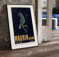 Green devil holding aperitif bottle print in a black frame leaning beside a vintage door on parquet