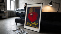 Bearded man with fur hat print in a slim black frame leaning on a dark sofa in a concrete print studio