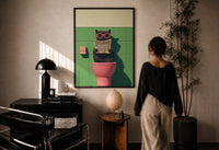 Cat on the Toilet Reading the Paper print in a black frame on a sunlit wall with a viewer