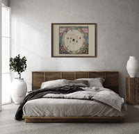 Antique celestial planisphere star chart print in a dark wood frame above a rattan bed on a plaster wall