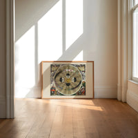 Copernican solar system celestial map print in an oak frame on a sunlit wood floor beneath tall window light