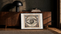 Ptolemaic celestial system with globe print in a black frame leaning against a walnut console in lamplight