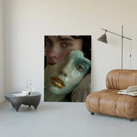 Large ceramic portrait art print leaning against a cream wall in a modern living room with leather chair