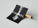 Chanel fashion print partially unrolled from cardboard shipping tube on gray surface, angled view