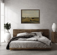 Peasant woman in harvest field print in a dark wood frame above a rattan bed on a plaster wall