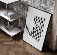 Hand waving checkered racing flag poster in a black frame leaning beside a shelf in a raw-plaster loft
