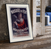 Man in red cloak holding iron mask print in a black frame leaning beside a vintage door on parquet