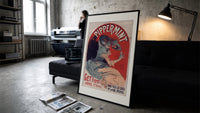 Woman pouring liqueur into glass print in a slim black frame leaning on a dark sofa in a concrete print studio