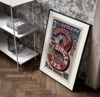 Woman using Singer sewing machine poster in a black frame leaning beside a shelf in a raw-plaster loft
