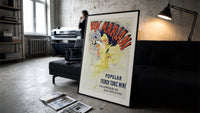 Woman dancing pouring wine print in a slim black frame leaning on a dark sofa in a concrete print studio