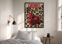 Cherries on Leopard print in a black frame above a bed with striped linens, a brass wall lamp and a sunlit window