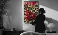 Cherries on Leopard print in a slim black frame being hung on a sunlit wall in a monochrome room