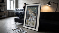 Woman blowing soap bubbles print in a slim black frame leaning on a dark sofa in a concrete print studio