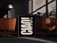 Black-framed Ciao print on the floor in front of a dark wooden console