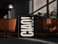 Black-framed Ciao White on Black print on the floor in front of a dark wooden console