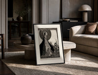 ethereal woman and shrouded man print in a black frame leaning on a travertine table in a sunlit lounge