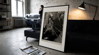 chained man in dungeon catacomb print in a slim black frame leaning on a dark sofa in a concrete print studio