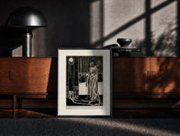 Black-framed Cloaked skeletal masque figure standing print on a moody console with designer coffee-table books