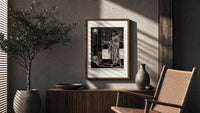 Cloaked skeletal masque figure standing poster framed above a fluted sideboard beside an olive tree