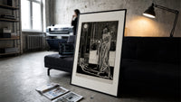 Cloaked skeletal masque figure standing print in a slim black frame leaning on a dark sofa in a concrete print studio