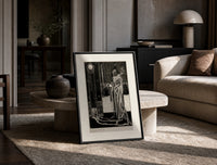 Cloaked skeletal masque figure standing print in a black frame leaning on a travertine table in a sunlit lounge