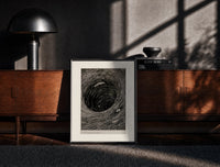 Black-framed Boat caught in whirlpool vortex print on a moody console with designer coffee-table books