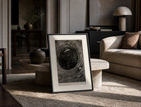 Boat caught in whirlpool vortex print in a black frame leaning on a travertine table in a sunlit lounge