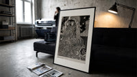 Two ornately robed figures embracing print in a slim black frame leaning on a dark sofa in a concrete print studio