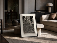 Two ornately robed figures embracing print in a black frame leaning on a travertine table in a sunlit lounge