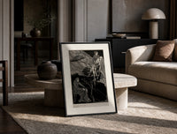 Man carrying pale woman, seated figure print in a black frame leaning on a travertine table in a sunlit lounge