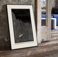 Two figures in boat amid rocks print in a black frame leaning beside a vintage door on parquet