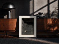 Black-framed Two figures in boat amid rocks print on a moody console with designer coffee-table books