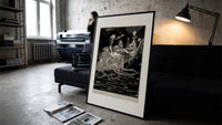 grotesque figures gathered around fantastical scene print in a slim black frame leaning on a dark sofa in a concrete…