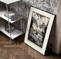 Mountain valley landscape with figure poster in a black frame leaning beside a shelf in a raw-plaster loft