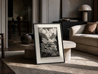 Mountain valley landscape with figure print in a black frame leaning on a travertine table in a sunlit lounge