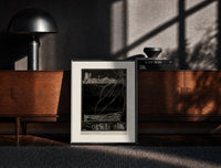 Black-framed Buried man in coffin underground print on a moody console with designer coffee-table books