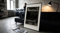 Buried man in coffin underground print in a slim black frame leaning on a dark sofa in a concrete print studio