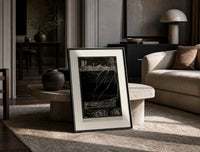 Buried man in coffin underground print in a black frame leaning on a travertine table in a sunlit lounge
